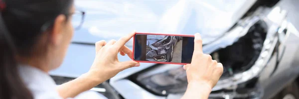 Woman agent takes pictures of damage to car after accident by smartphone