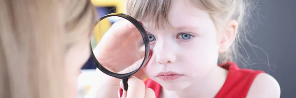Arzt untersucht Auge des kleinen Mädchens durch Lupe — Stockfoto