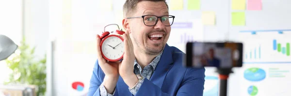 빨간 알람 시계를 들고 교육용 비디오를 녹화하고 있는 남성 블로거 — 스톡 사진