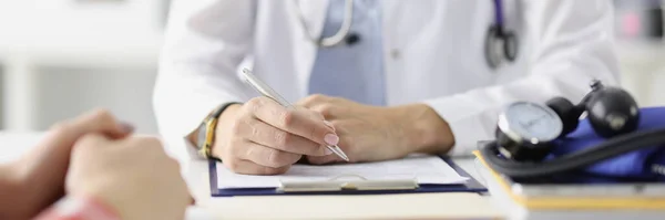 Médico sentado à mesa e preparando registros médicos com caneta esferográfica close-up — Fotografia de Stock