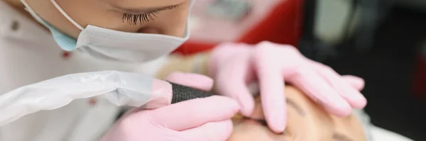 Master in beschermende medische masker maken van permanente oog make-up aan cliënt in schoonheidssalon — Stockfoto