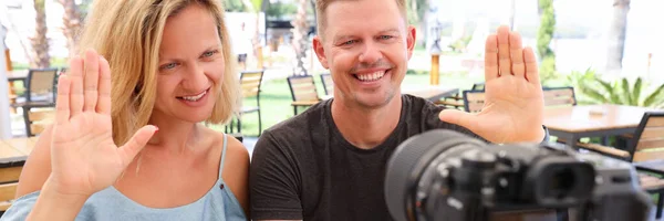 Man en vrouw zitten aan tafel in de bar en zwaaien naar de camera — Stockfoto