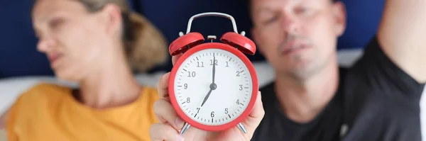 Сонный мужчина и женщина лежат в постели и держат красный будильник крупным планом — стоковое фото