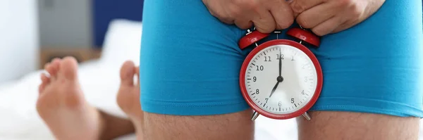 Hombre sosteniendo el despertador cerca de los genitales contra el fondo de las piernas femeninas tumbadas de cerca —  Fotos de Stock