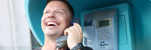 Jovem sorridente falando na cabine telefônica na rua — Fotografia de Stock