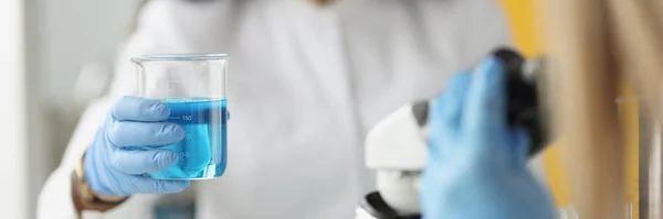 医学的または科学的研究者の女性は、実験室で明確な青色のソリューションを持つ試験管を見て — ストック写真