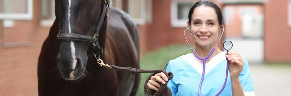 Veterinário fêmea detém estetoscópio e fica ao lado de close-up cavalo — Fotografia de Stock