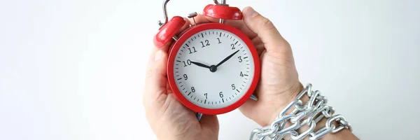 Male hands are tied with chain and hold red alarm clock closeup — Stock Photo, Image