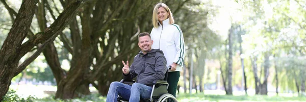 Kobieta spacerująca w parku z niepełnosprawnym mężczyzną na wózku inwalidzkim — Zdjęcie stockowe