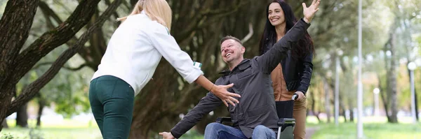Disabled man in wheelchair walking in park with nurse and hugging his girlfriend — Stock Photo, Image