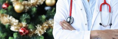 Steteskoplu kadın doktor Noel ağacının yanında duruyor.