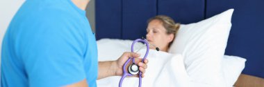 Doktor hasta yatağında oturuyor ve elinde steteskop tutuyor.