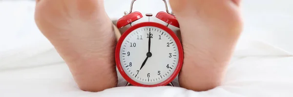 Red alarm clock standing in bed between female heels closeup — Foto Stock