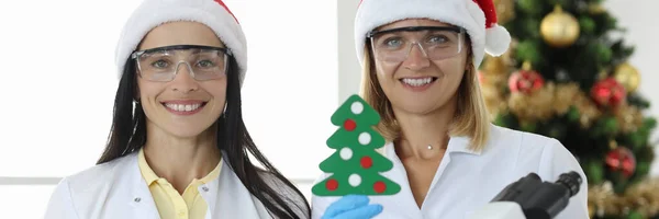 Twee wetenschappelijke werkers houden kolven en microscoop tegen de achtergrond van de kerstboom — Stockfoto