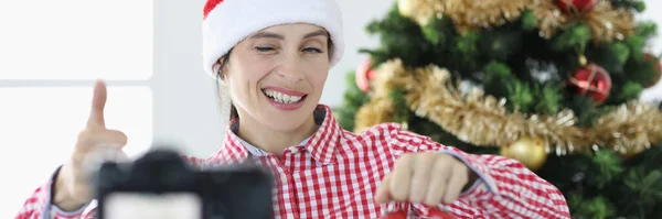 Jonge vrouw blogger in santa claus hoed houdt wekker en knipogen op camera — Stockfoto