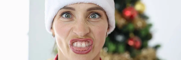 Portré irritált nő télapó claus kalap hátterében karácsonyfa — Stock Fotó