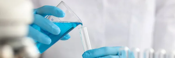 Científico con guantes vierte líquido azul en tubo de ensayo en laboratorio — Foto de Stock