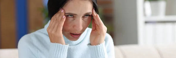 Femme avec mal de tête tient les mains aux tempes tout en étant assis sur le canapé — Photo