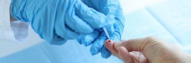 Tek kullanımlık eldiven giyen doktor hasta parmağından kan alır.