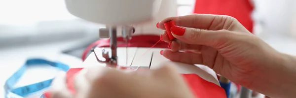 Mãos femininas linha vermelha em uma máquina de costura — Fotografia de Stock