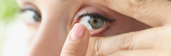 Woman puts on soft contact lens over eyes closeup
