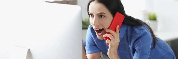 Jovem mulher chocada falando no smartphone e olhando para o monitor do computador — Fotografia de Stock