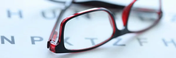 Стильные очки в черно-красных обрамлениях лежат на офтальмологическом столе вблизи — стоковое фото