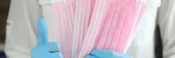 Dokter in handschoenen houdt medisch masker en duimen up close-up — Stockfoto