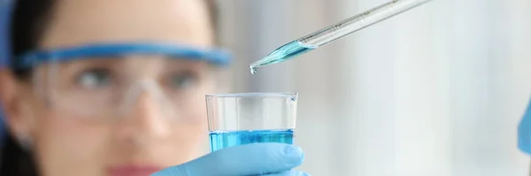 청색 액체로 된 플라스크로 물방울을 뚝뚝 떨어지게 하는 여성 과학자 — 스톡 사진