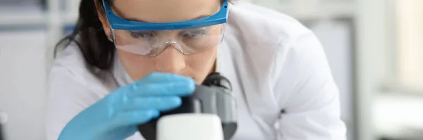 Młoda kobieta naukowiec w okularach patrzy przez mikroskop zbliżenie — Zdjęcie stockowe