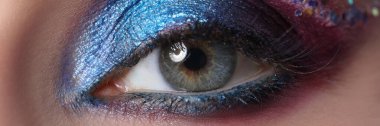 Parlak mavi göz kapağı makyajı ve çok renkli ışıltılar.