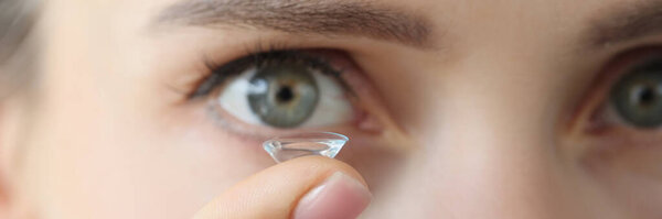 Soft contact lens on female finger against background of female eyes