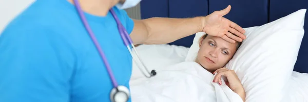 Dokter houdt hand op het voorhoofd van een liegende vrouw op bed met koorts — Stockfoto