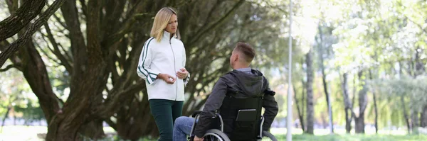 Genç bir kadın tekerlekli sandalyedeki adamla parkta iletişim kuruyor. — Stok fotoğraf