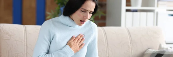 Young woman sitting on couch and coughing — Stock Photo, Image