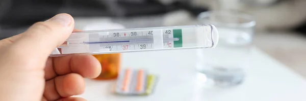 Man hand houdt medische thermometer met temperatuur op de achtergrond van zieke vrouw liggend op couh — Stockfoto