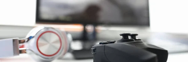 Game joystick with headphones lie on table with computer monitor closeup — Stock Photo, Image