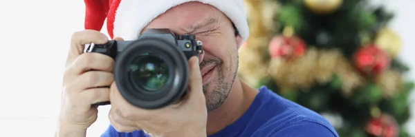 Mężczyzna w czerwonym kapeluszu Mikołaja robi zdjęcia aparatem w pobliżu choinki — Zdjęcie stockowe