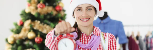 Naaister in rood Kerstman hoed met wekker en schaar in de buurt van kerstboom — Stockfoto