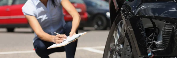 Kvinnlig inspektör skriver i dokument på urklipp nära trasiga bil. Bilförsäkring — Stockfoto