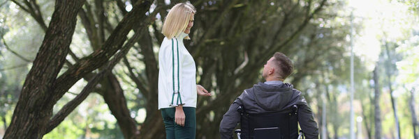 Young smiling woman walks in park with man in wheelchair