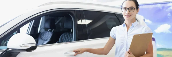 Молода жінка з документами на руках тримає двері автомобіля в салоні — стокове фото