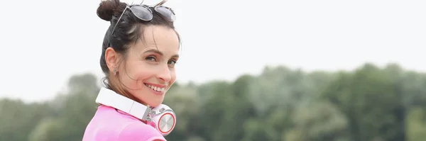 Молода усміхнена жінка з навушниками на шиї стоїть на мосту — стокове фото