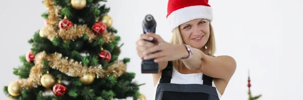 Noel Baba şapkalı kadın Noel ağacının yanında elektrikli matkap tutuyor. — Stok fotoğraf