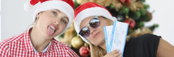 Noel Baba şapkalı kadınlar yılbaşı ağacı yakınında uçak bileti tutuyorlar. — Stok fotoğraf
