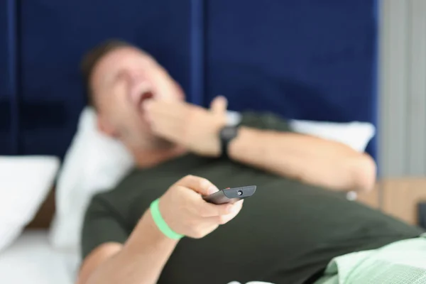 Yawning man is holding remote control closeup — Stok Foto