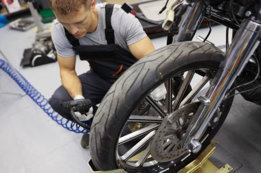 Garajda, tulumlu bir tamirci motosikletin yanında oturuyor.