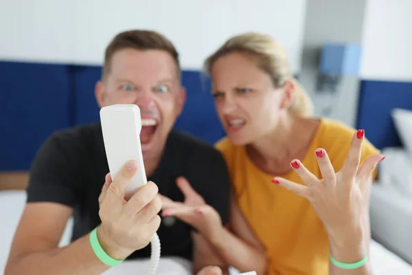 Paar brüllt ins Telefon, während es im Hotel auf dem Bett sitzt — Stockfoto