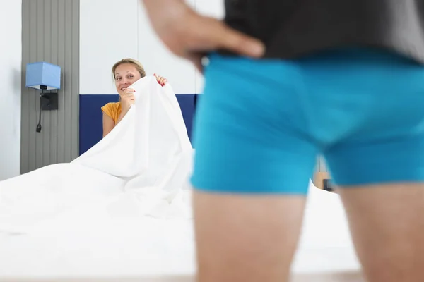 Un hombre en pantalones cortos azules se para frente a una mujer en una cama de hotel —  Fotos de Stock