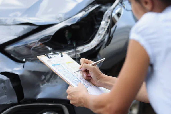 Eine Frau an einem kaputten Auto füllt ein Dokument aus, verschwommen — Stockfoto